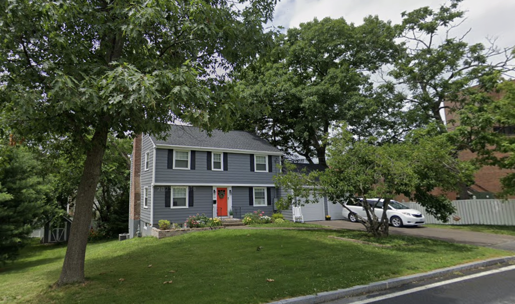 After: the same colonial home refreshed with new blue-gray siding, a red front door and tidy landscaping