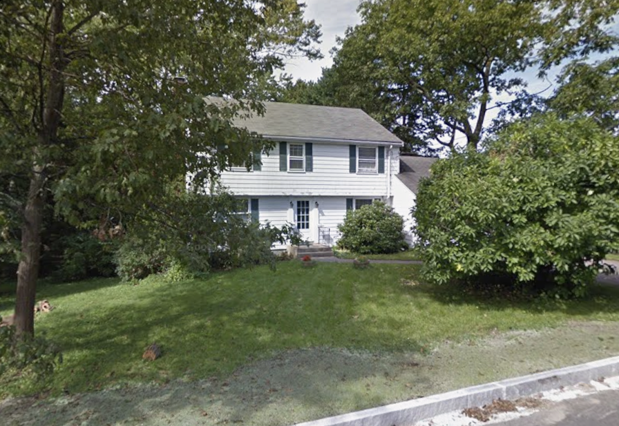 Before: a worn, dated white colonial home with overgrown landscaping and peeling paint