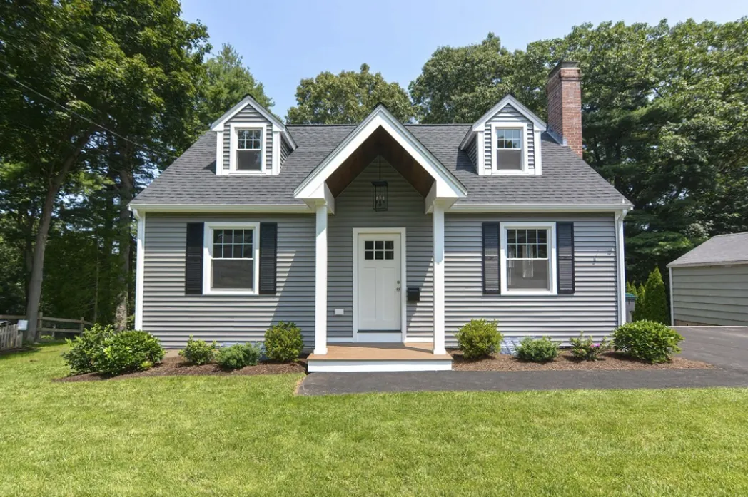 After: the same Cape Cod home fully renovated with fresh gray siding, white trim, a new roof and clean landscaping