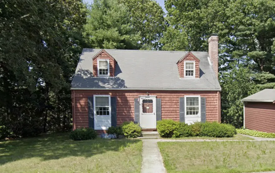Before: a dated red-shingled Cape Cod style home with worn siding and overgrown shrubs